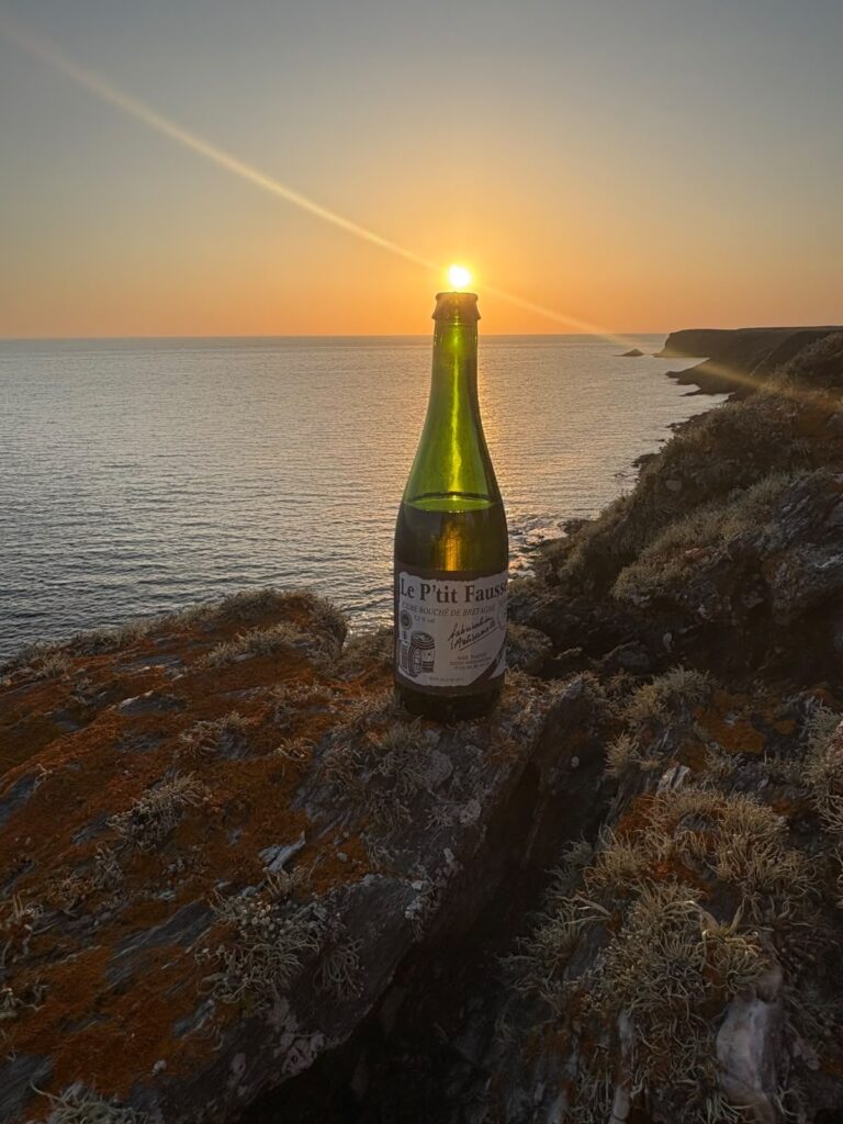Bouteille de cidre Le P'tit Fausset sur des rochers au coucher de soleil face à la côte
