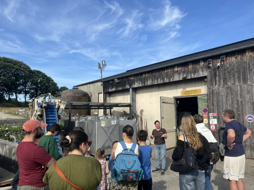 Groupe en visite guidée devant l'atelier de production du P'tit Fausset, enseigne jaune et équipements extérieurs